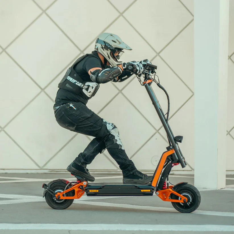 Person riding an electric scooter with a helmet and protective gear on a tiled floor.
