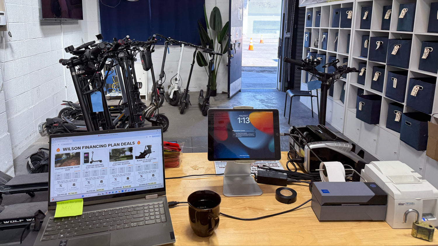 Workstation with laptop, monitor, and printer in a room with shelves and equipment.