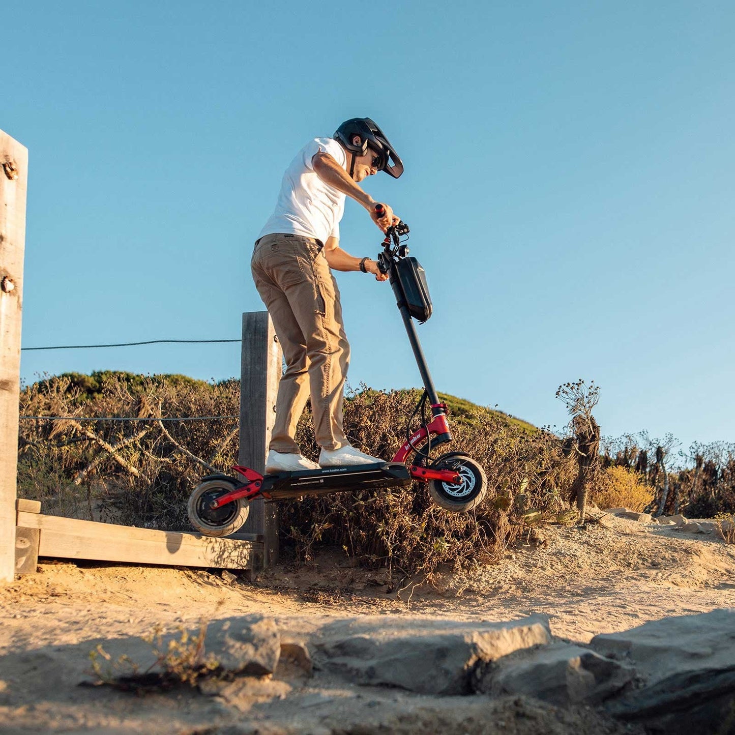 Person riding a red electric scooter in an urban setting with trees and buildings in the background.