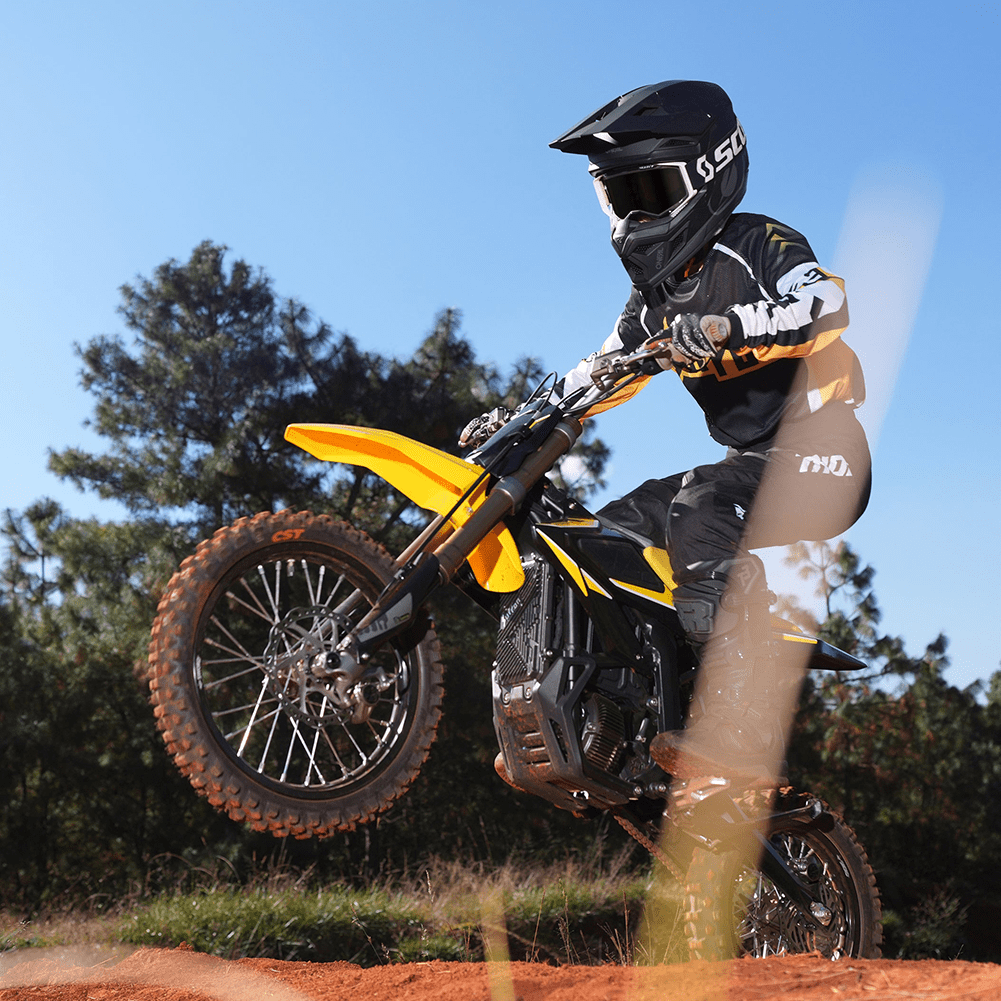 Person riding a yellow dirt bike on a dirt track with trees in the background