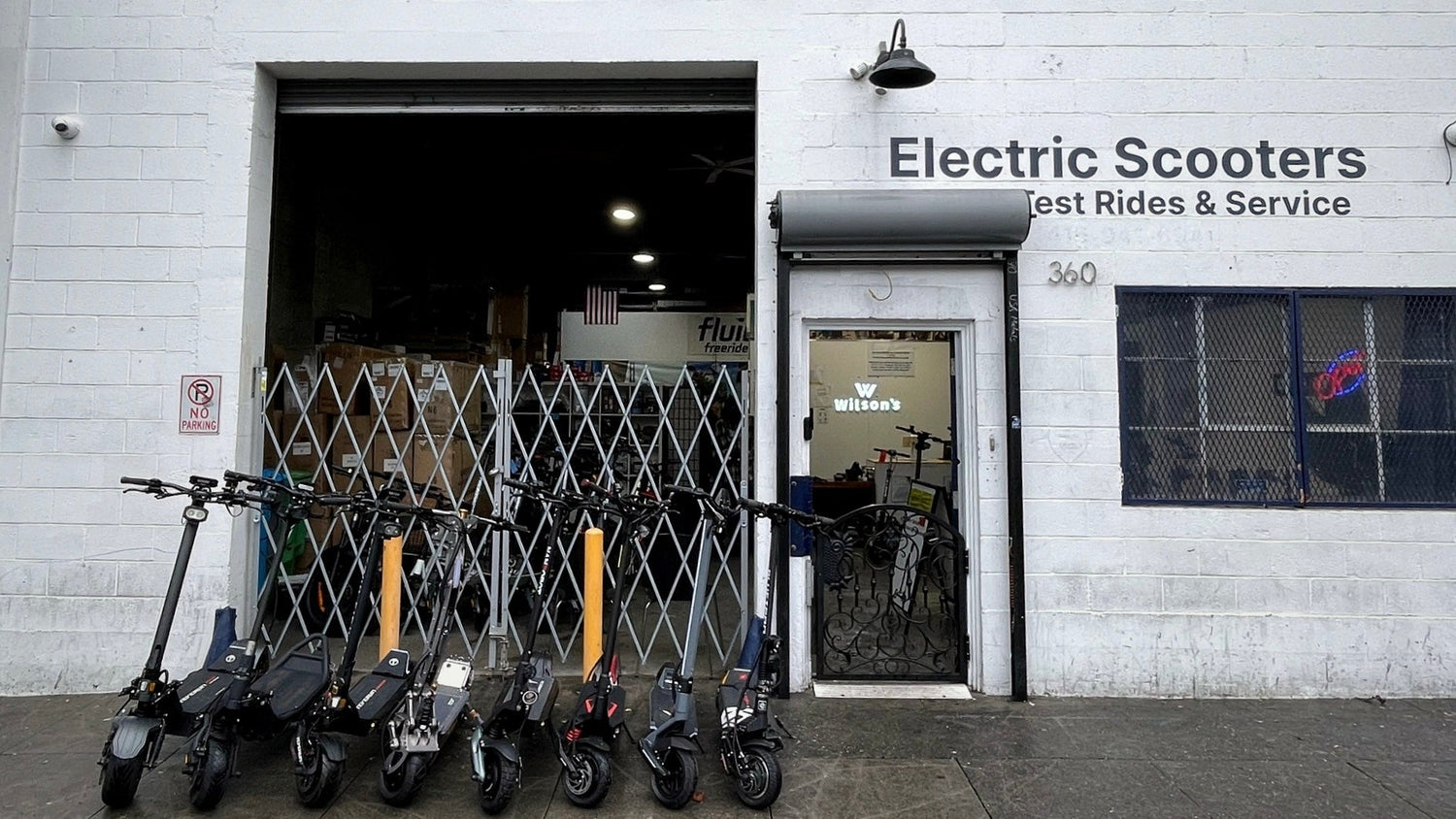 Electric scooters lined up outside a building with 'Electric Scooters Test Rides & Service' sign.